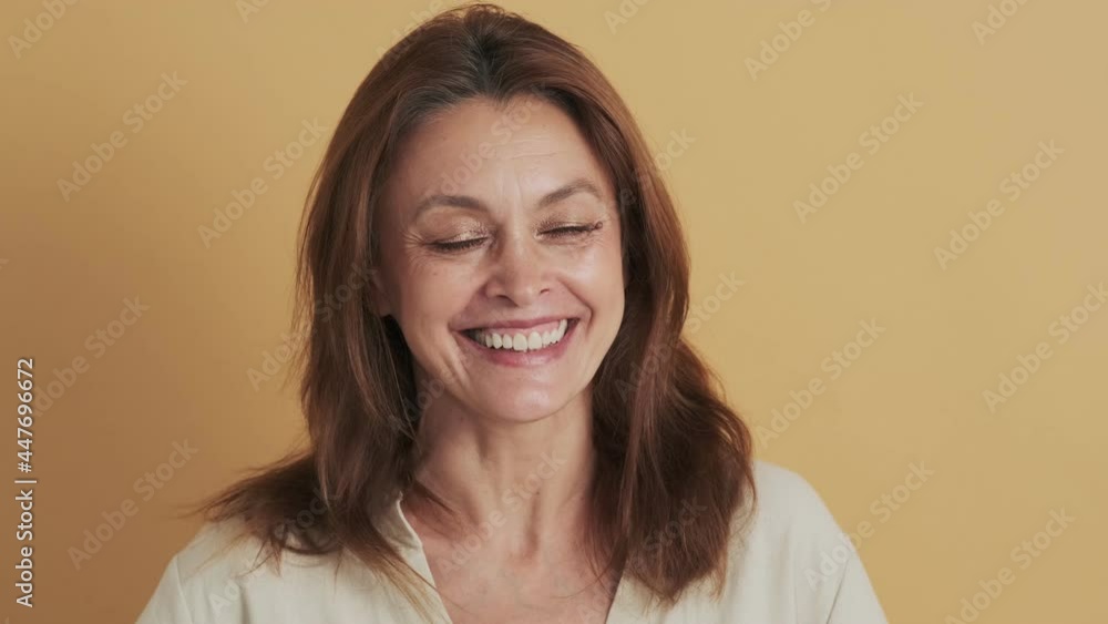 A happy middle-aged brunette woman laughing standing isolated over beige background in the studio A happy middle-aged brunette woman laughing standing isolated over beige background in the studio