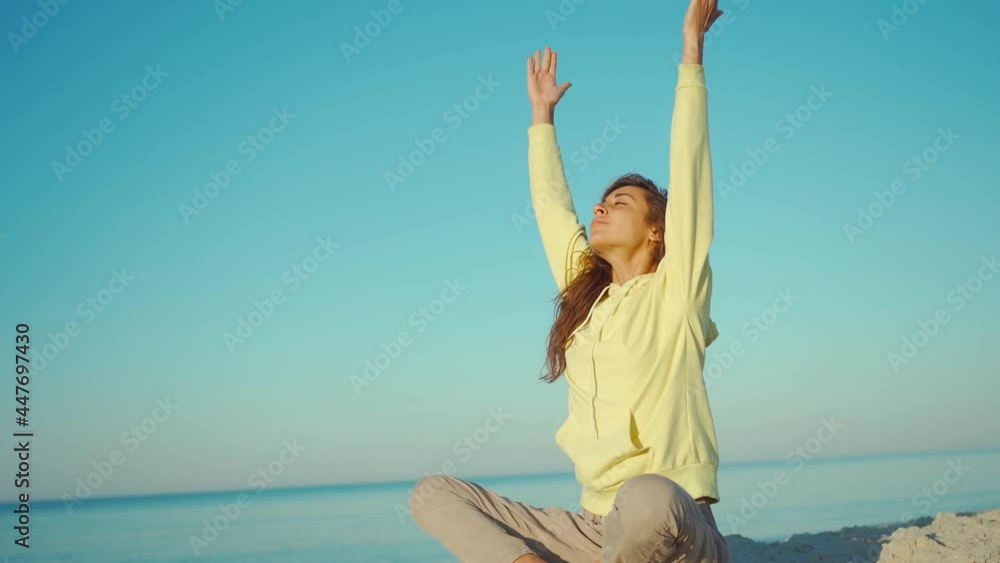 beautiful calm brunette woman in yellow hoodie meditating and doing yoga practice on beautiful calm sea beach at sunrise beautiful calm brunette woman in yellow hoodie meditating and doing yoga practice on beautiful calm sea beach at sunrise