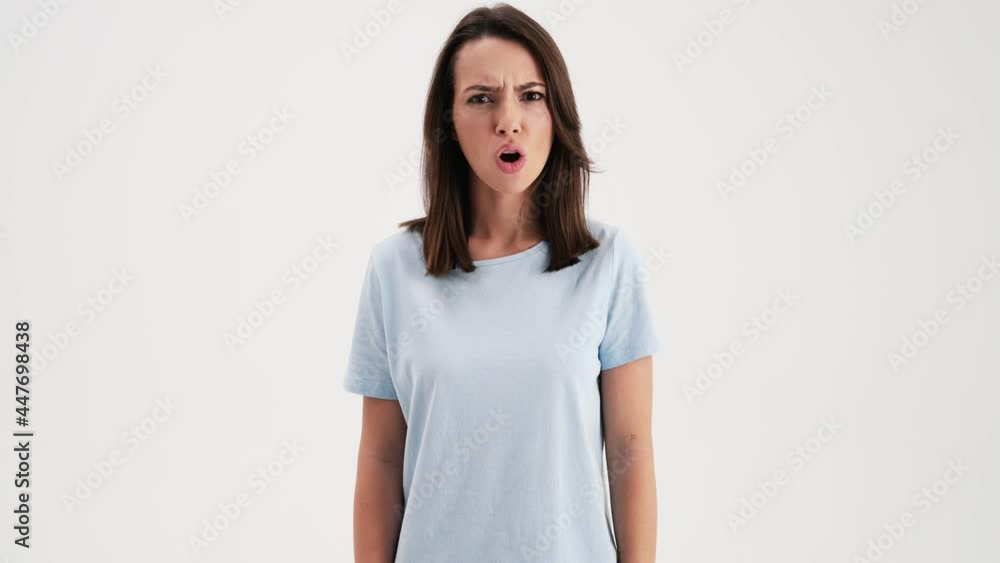 A displeased angry woman wearing basic t-shirt is doing negative gesture giving negative answer standing in the studio isolated over white background A displeased angry woman wearing basic t-shirt is doing negative gesture giving negative answer standing in the studio isolated over white background