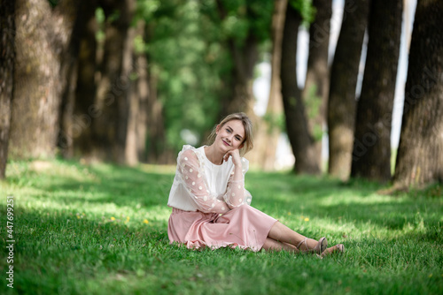 Summer portrait of a young girl in a pink dress in green avenue of trees spot of ligh on the grass