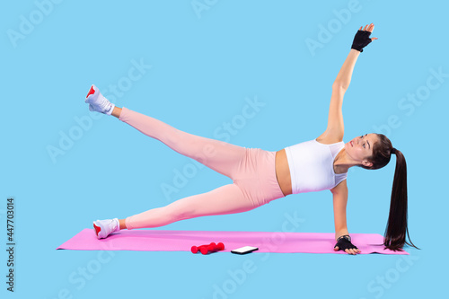 Female trainer wearing light sports clothes making fitness exercises on the mat raising an arm and a leg at the same time.