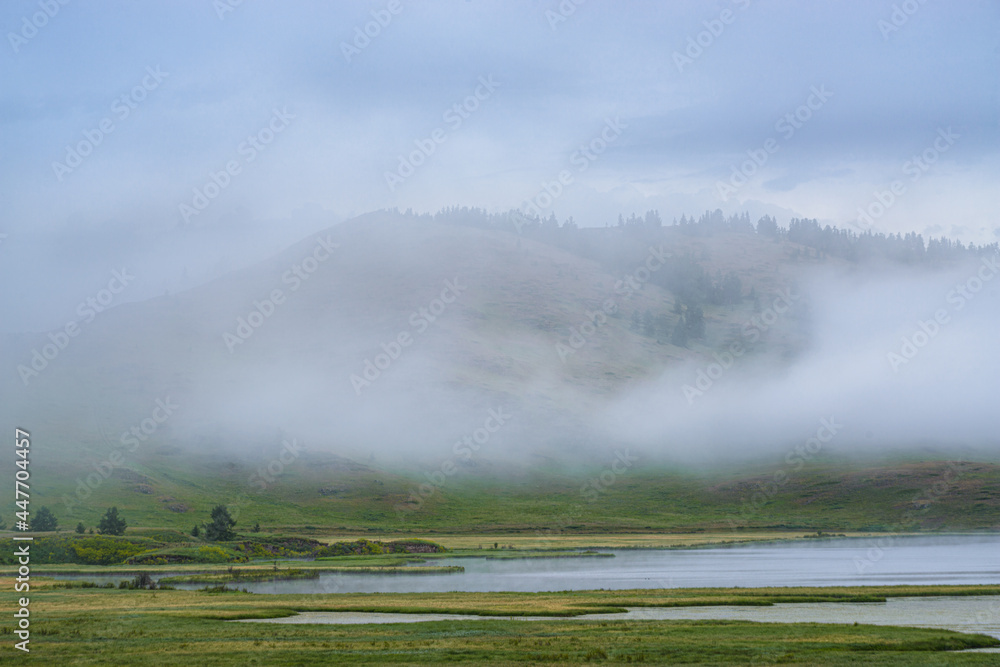 picturesque view of lake near hill in foggy morning 