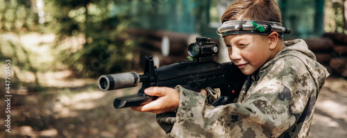 Boy looking into the optical sight a weapon. Children playing laser tag shooting game in outdoor. War simulation game. Banner