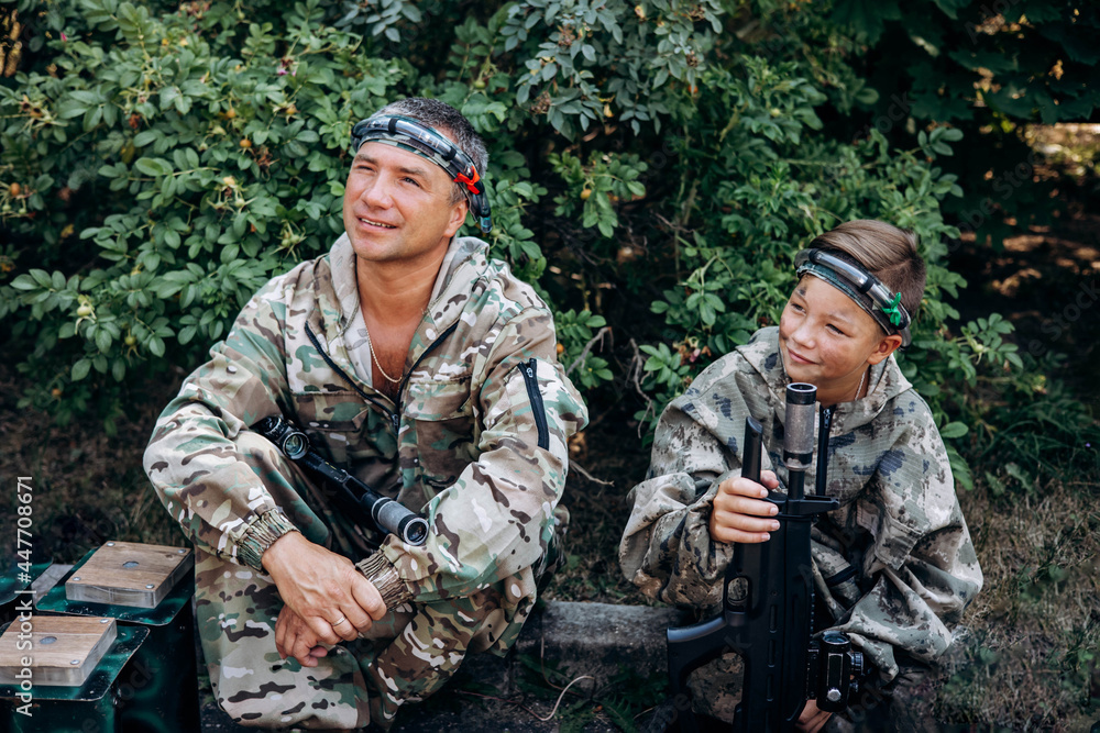 Father and son in camouflage ready to play in laser tag shooting game with a weapon outdoor