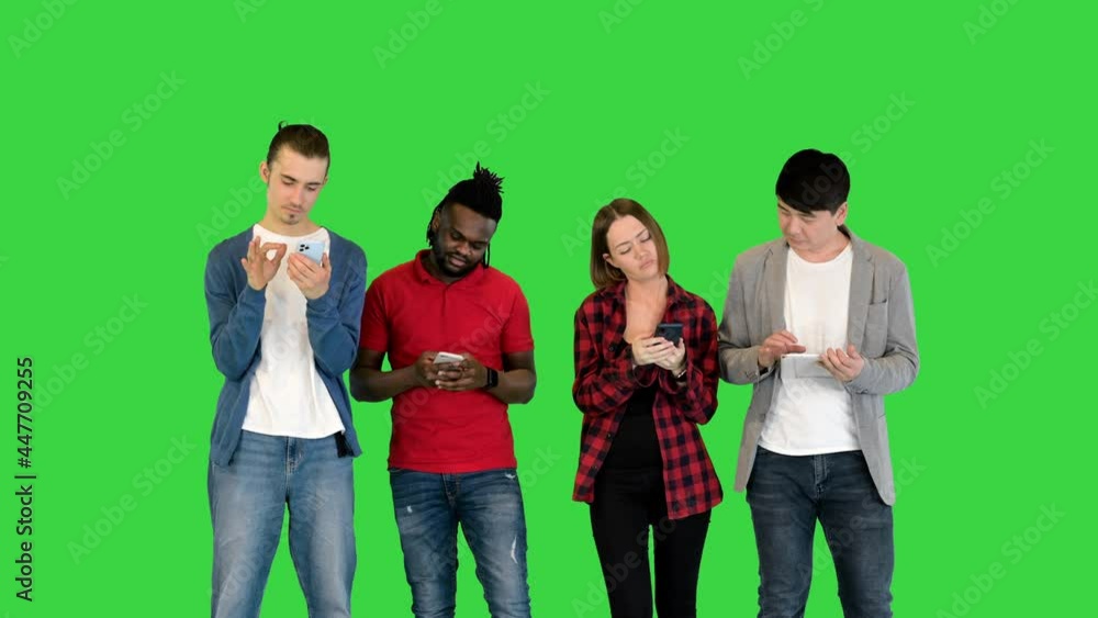 Young friends stand in front of camera, focused on their gadgets on a Green Screen, Chroma Key. Young friends stand in front of camera, focused on their gadgets on a Green Screen, Chroma Key.