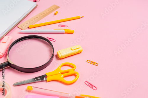 Education and business. Composition with magnifier, copybook and yellow office supplies on pink background. Close up. Copy space. Concept of back to school