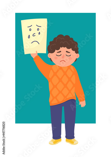 Sad boy holds piece of paper with drawn sad face. Emotional development, empathy concepts.