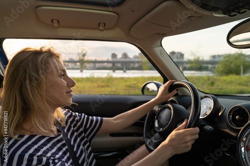 Happy smiling woman driving modern vehicle. Caucasian female sitting alone on driver seat with fasten belt. Attractive confident blonde travelling by car. Lifestyle and success concept © DimaBerlin