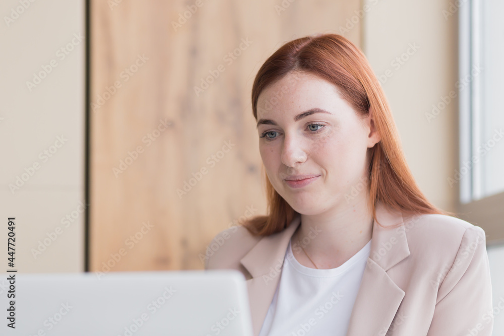 Close-up photo of a red haired business woman smiling while sitting at a computer, got a satisfactory result Close-up photo of a red haired business woman smiling while sitting at a computer, got a satisfactory result