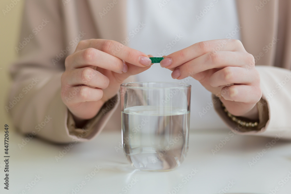the woman's hands open the tablet in half, and dilute the medicine with a glass of water the woman's hands open the tablet in half, and dilute the medicine with a glass of water
