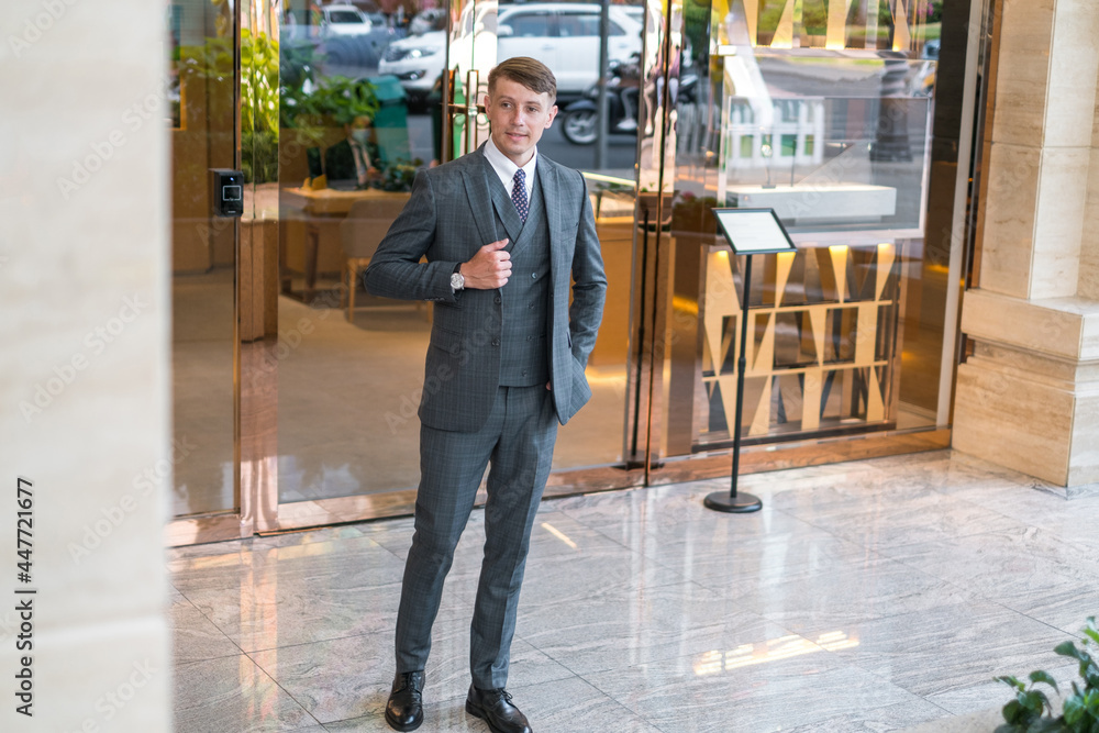 Obraz premium Portrait of successful young businessman in grey suit standing near modern buiding.
