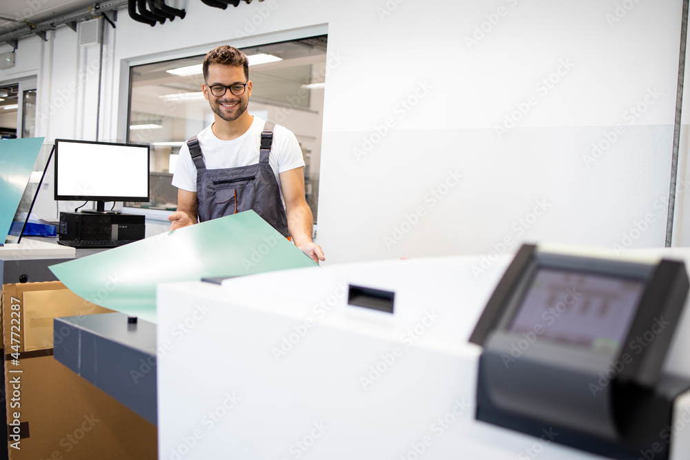 Smiling print worker operating computer to plate machine in print shop.