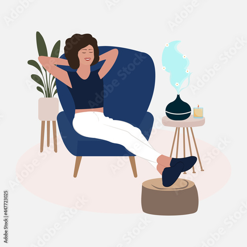 Aromatherapy Concept. Woman relaxing on the armchair while enjoying the aromatherapy in a minimalist living room. Home relaxation with aromatherapy from oil diffuser with flower smell.