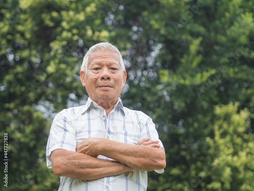 Fototapeta Naklejka Na Ścianę i Meble -  Portrait of an elderly Asian man with short gray hair smiling and looking at the camera while standing in a garden. Aged people and healthcare concept