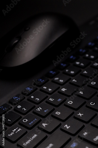 Image of black elegant portable wireless keyboard and mouse which is focused in the QWERTY letters in vertical and black background