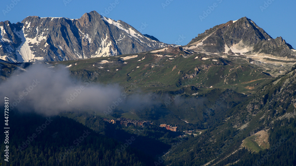 Mountain landscape. Snow-capped rocky peak with clouds and fog around.