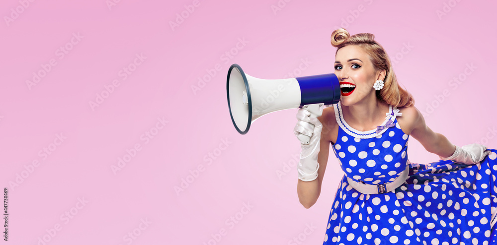 Φωτογραφία Image of woman holding megaphone, dressed in pin up style blue dress in polka dot white gloves, over pink colour background