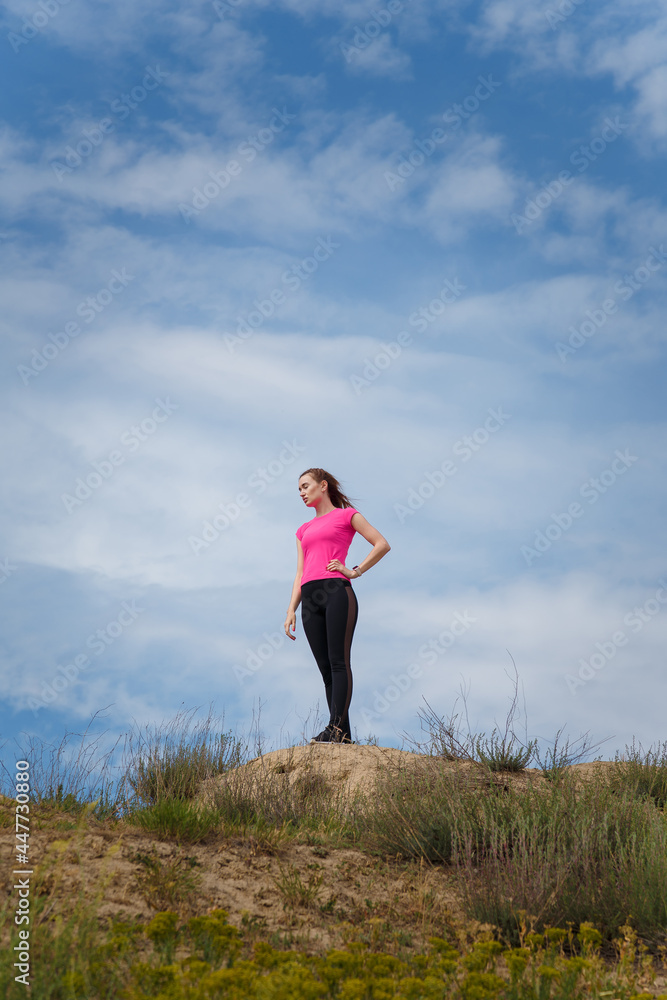 Young woman in sportswear standing on hill top on blue sky background. Fitness, healthy way of life, wellbeing, freedom, mental health, triumph, winning concept. Young woman in sportswear standing on hill top on blue sky background. Fitness, healthy way of life, wellbeing, freedom, mental health, triumph, winning concept.