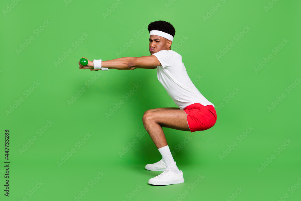 Fototapeta premium Full length photo of serious tired dark skin man wear white t-shirt squatting with dumbbells isolated green color background