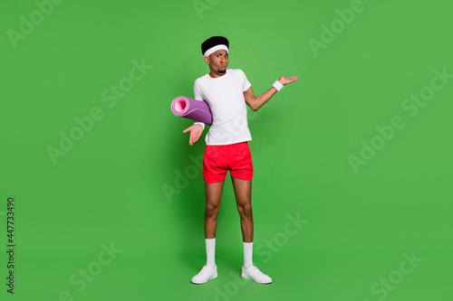 Full length photo of doubtful unsure dark skin guy dressed sport outfit shrugging shoulders isolated green color background © deagreez