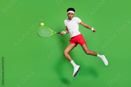 Full length photo of funky serious dark skin man wear white t-shirt jumping high playing squash isolated green color background