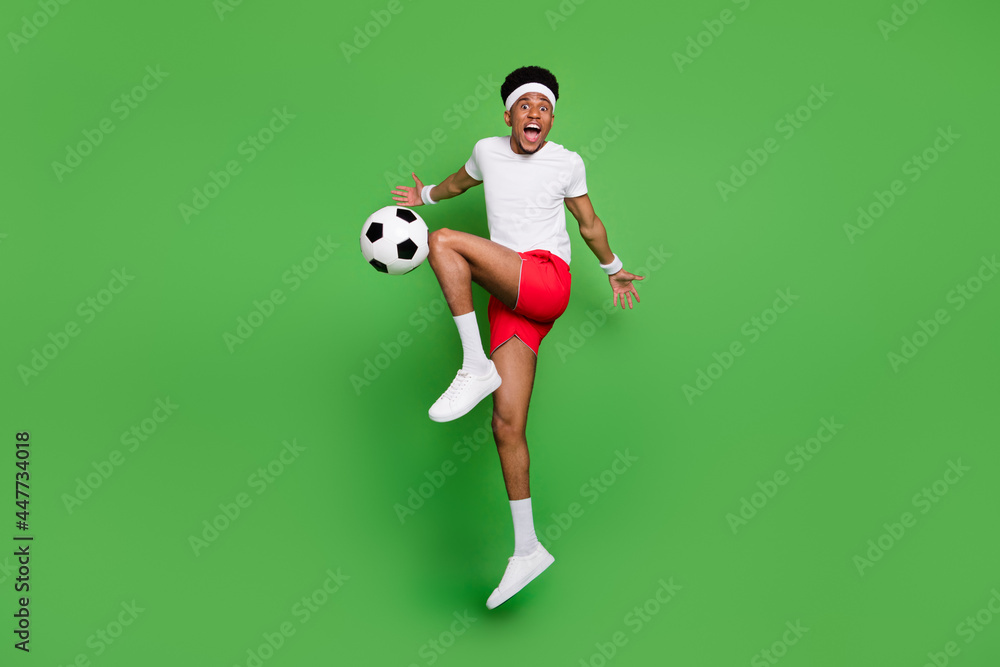 Fototapeta premium Full length body size view of trendy handsome cheery sportsman jumping playing soccer isolated over bright green color background