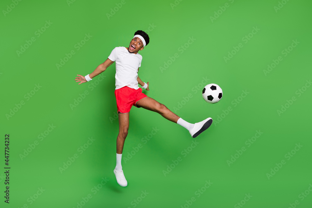 Photo of energetic guy jump open mouth leg hit ball wear white t-shirt shorts footwear isolated green color background