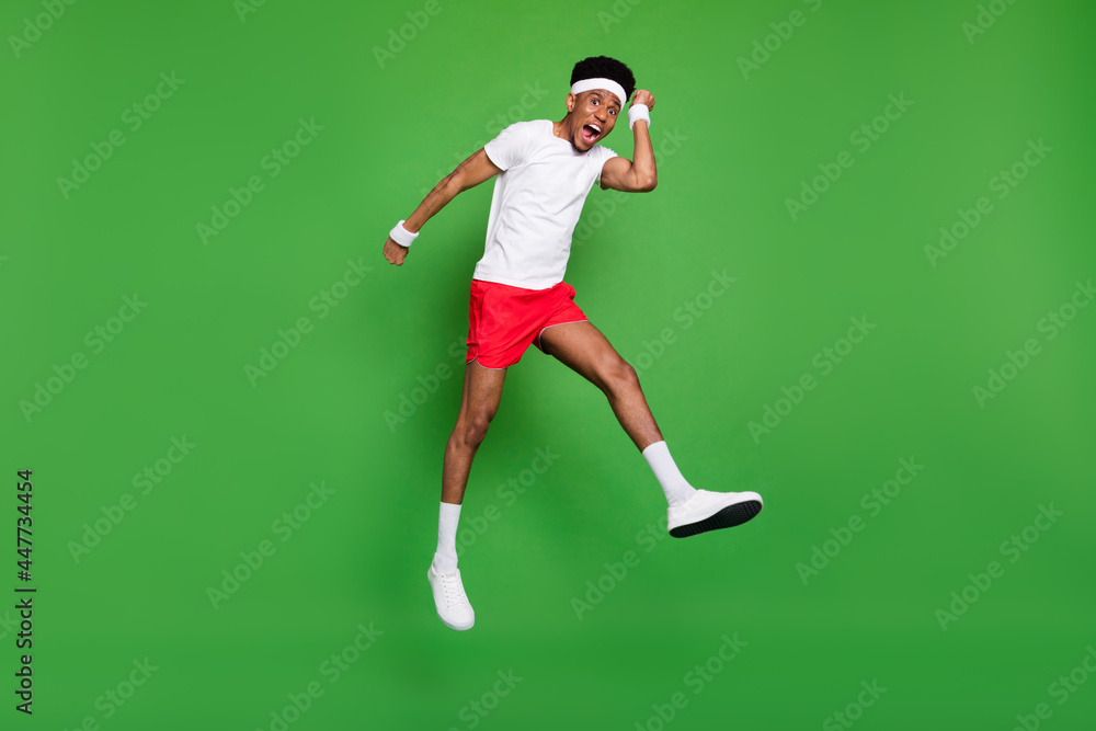 Full length photo of lucky funky dark skin guy dressed sport outfit jumping high rising fists isolated green color background