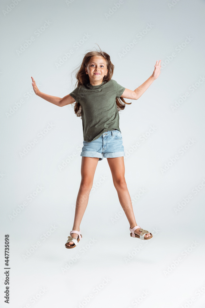 Full-length portrait of of beautiful preschool smiling girl jumping, playing isolated on gray studio background. Copyspace for ad. Childhood, education, emotion concept Full-length portrait of of beautiful preschool smiling girl jumping, playing isolated on gray studio background. Copyspace for ad. Childhood, education, emotion concept