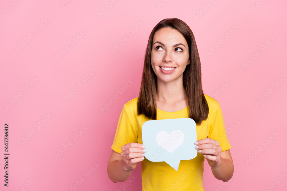 Photo of pretty adorable young woman dressed yellow t-shirt looking empty space holding heart icon isolated pink color background Photo of pretty adorable young woman dressed yellow t-shirt looking empty space holding heart icon isolated pink color background