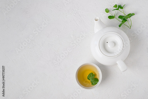 Herbal mint tea in white ceramic teapot and white cup and mint stalks on white background,  top view, copy space. Serving for the tea ceremony