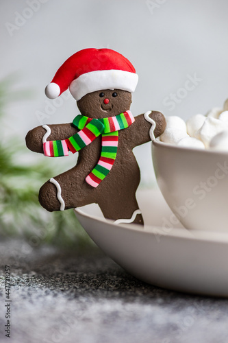 Christmas Gingerbread man in a santa hat cookie next to a cup of mini marshmallows photo