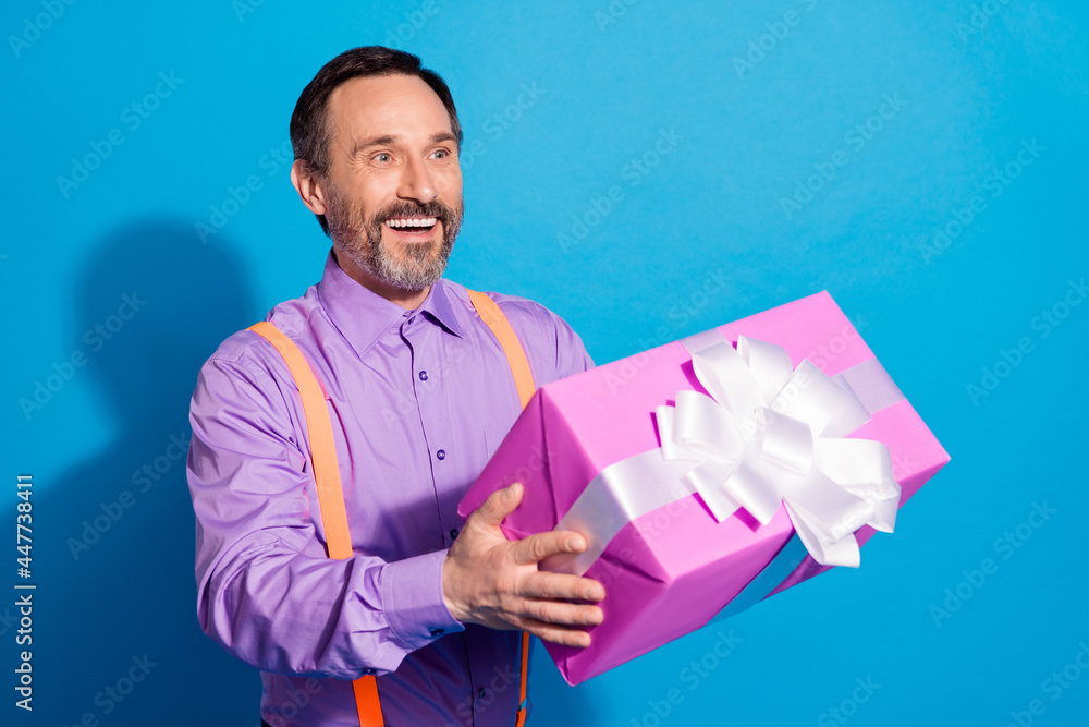 Profile side photo of mature man happy positive smile hold present box birthday isolated over blue color background Profile side photo of mature man happy positive smile hold present box birthday isolated over blue color background