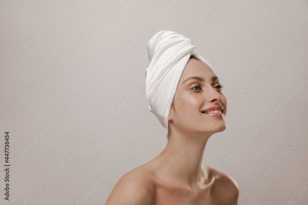 Joyful young lady with white towel wrapped hair and naked shoulders, smiling, looking aside at free space. Skincare and beauty concept Joyful young lady with white towel wrapped hair and naked shoulders, smiling, looking aside at free space. Skincare and beauty concept