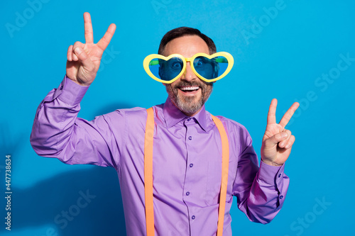 Photo of mature man happy positive smile show peace cool v-sign wear sunglass isolated over blue color background