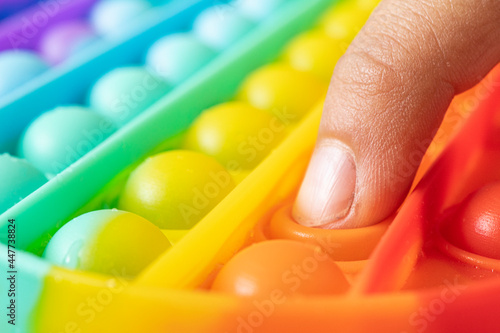 Macro of hands with Pop It sensory antistress. Kid play colorful rainbow pop it sensory toy, hands close-up. Concept of pop it sensory game for stressed child. photo