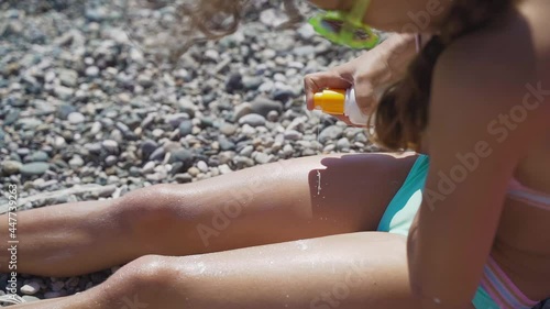 Little girl with glasses on the beach sunbathes and smears her skin with sunscreen. Kid draws on his feet with sun lotion. Travel concept, rest, vacation, tourism