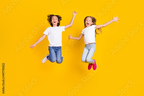 Full length body size view of two nice crazy cheerful carefree kids jumping having fun fooling isolated over bright yellow color background