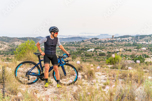 Professional cyclist with sportswear and helmet looking at the landscape on sunny day with his road bike