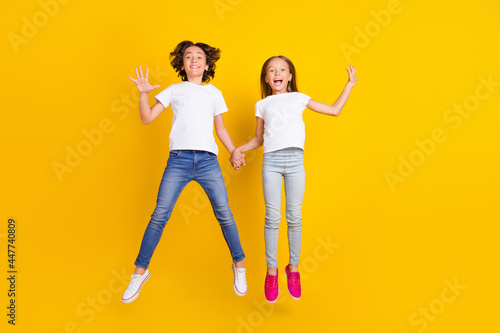 Full length body size view of two attractive cheerful kids jumping having fun isolated over bright yellow color background
