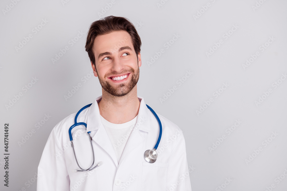 Photo of professional positive young doc man dressed white coat smiling looking empty space isolated grey color background Photo of professional positive young doc man dressed white coat smiling looking empty space isolated grey color background