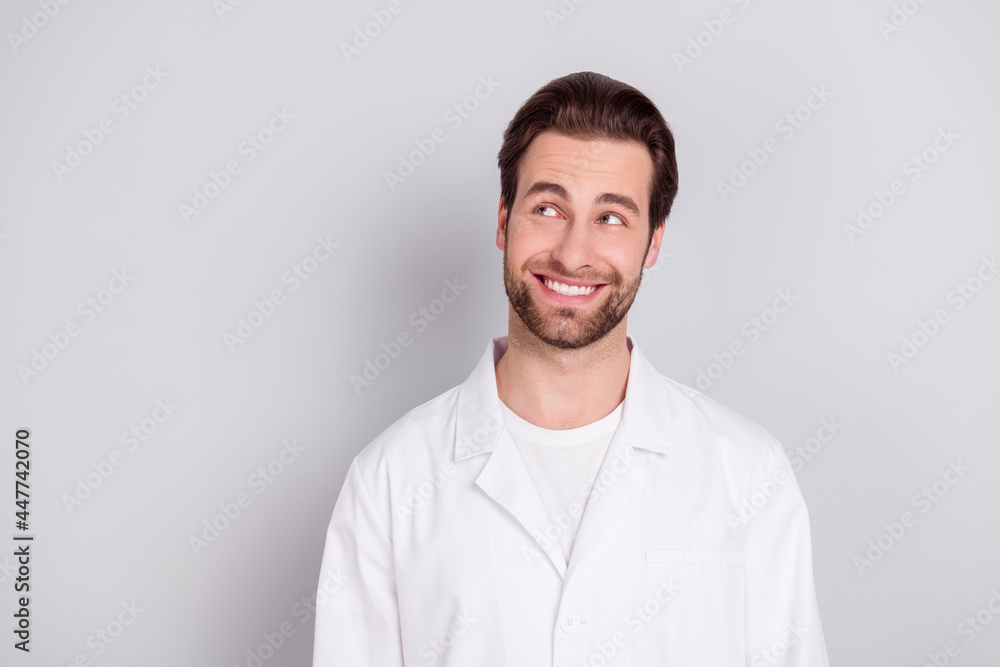 Photo of positive thoughtful young doc man dressed white coat smiling looking empty space isolated grey color background Photo of positive thoughtful young doc man dressed white coat smiling looking empty space isolated grey color background