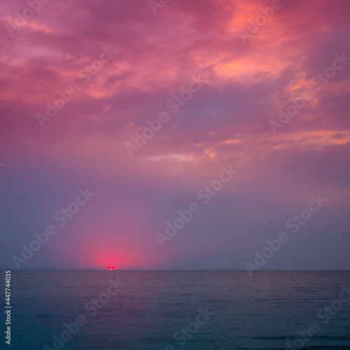 Dramatic cloudy sky at sunset on Cape Cod beach. Pink sun going down the sea. © Naya Na