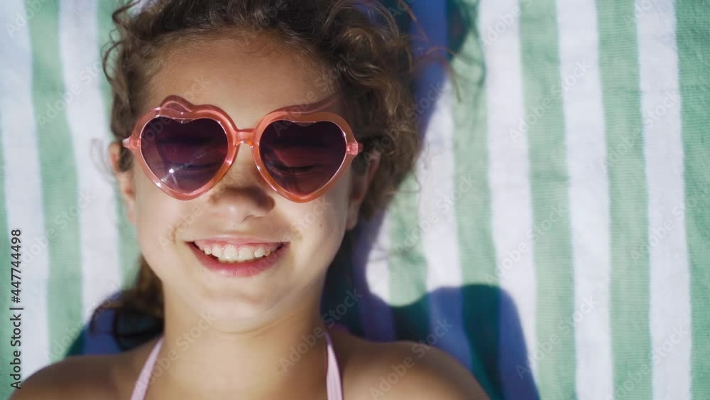 Cute girl in sunglasses sunbathing on the sea. Happy kid on the beach smiles and sunbathes. Portrait of a child on vacation, travel, tourism, vacation Cute girl in sunglasses sunbathing on the sea. Happy kid on the beach smiles and sunbathes. Portrait of a child on vacation, travel, tourism, vacation