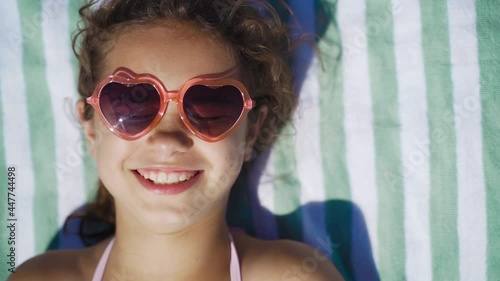 Cute girl in sunglasses sunbathing on the sea. Happy kid on the beach smiles and sunbathes. Portrait of a child on vacation, travel, tourism, vacation
