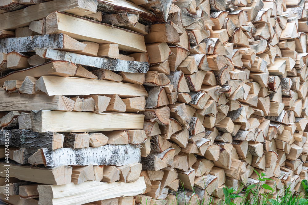stacked woodpile of birch firewood in nature in the village on a bright summer day. Close-up stacked woodpile of birch firewood in nature in the village on a bright summer day. Close-up