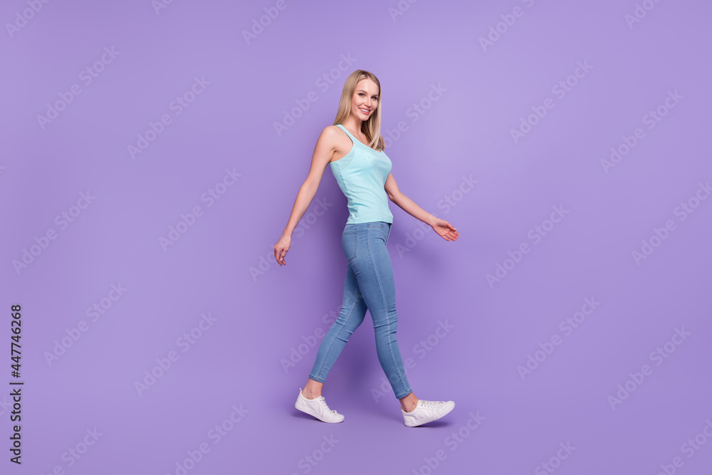 Full body profile photo of nice blond young lady go wear teal top jeans sneakers isolated on violet color background