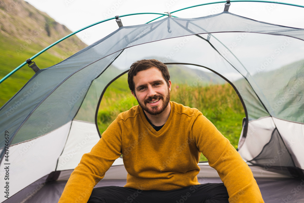 Young and attractive man sitting on his tent set up outdoors enjoying nature in Scotland while doing solo camping