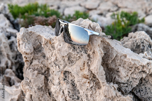 Reflet du phare du Cap Ferrat au soleil couchant dans des lunettes de soleil posées sur des roches  © Bernard