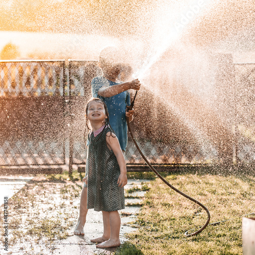 little children playing together with a garden hose on hot and sunny summer day on sunset